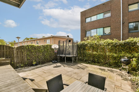a back yard with chairs and tables on it, in front of an apartment building there is a brick wall...