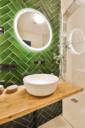 a bathroom with green tiles on the wall and wooden counter in front of the sink, which is surrounded...