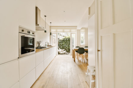 a kitchen and dining area in a house with white walls, wood flooring and an open door leading to the living roomの写真素材
