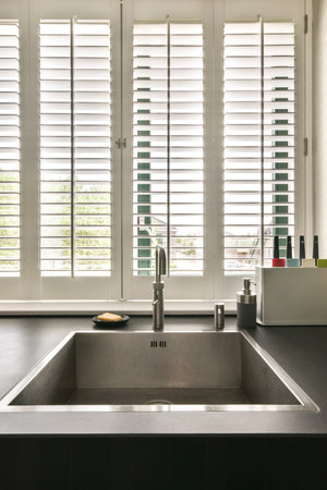 a kitchen sink and window with plantation shutters in the window behind it, which is open to let light into the roomの写真素材