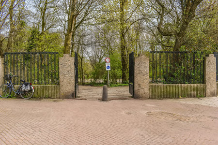 an iron gate in the middle of a park with bicycles parked on it and trees lining the path to the entranceの写真素材