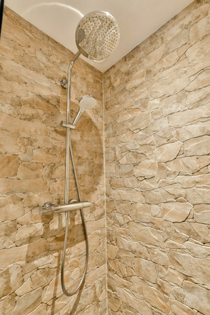 a shower that is in a bathroom with stone walls and tile on the wall next to it, there is a hand held showerの写真素材