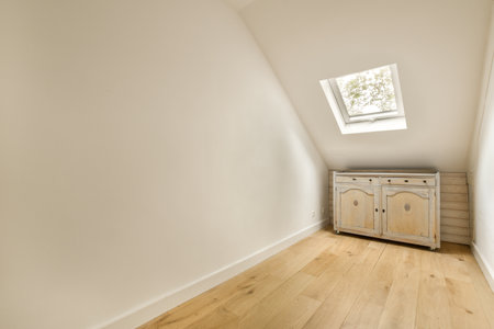 a white room with wood floors and a small cabinet in the corner on the right is an open skylight...