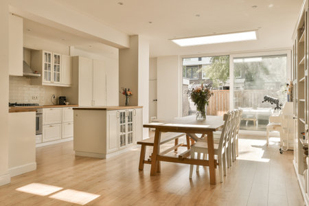 a kitchen and dining area in a house with white cabinets, wood flooring and an open door leading to the patioの写真素材