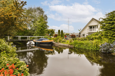 a canal with boats in the water and houses on both sides, surrounded by lush green trees and blue skyの写真素材