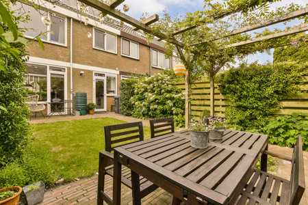 an outside area with a table, chairs and some plants on the lawn in front of a brick wall is behind
