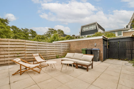 a patio with chairs and a fire pit in the middle of the yard, next to a fenced backyard area