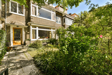 a house with trees and bushes in the front yard, as seen from the garden path leading up to the back...