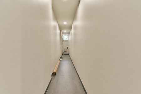 a long hallway with white walls and wood flooring on the right side, there is an empty bench in the middleの写真素材