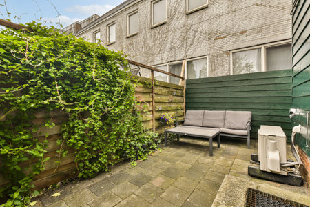 an outside area with some plants on the wall and a couch in the corner, next to a green fence
