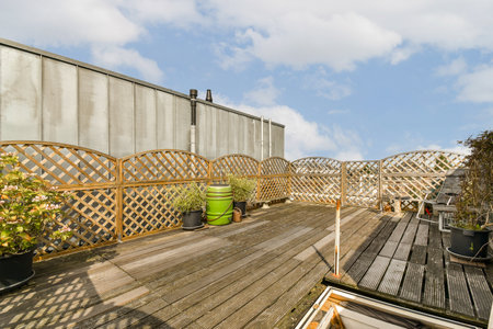 a wooden deck with pots and plants on the side, against a cloudy blue sky in the back ground