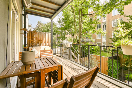 a balcony with two wooden chairs and a table on the left side, looking out to the trees in the...