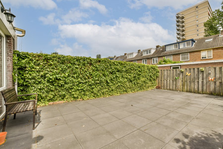 a backyard area with a fence, bench and some plants on the side of the house there is a blue sky in...