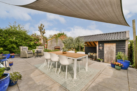 a patio area with chairs, tables and an umbrella over the dining table in front of a wooden shed behindの写真素材