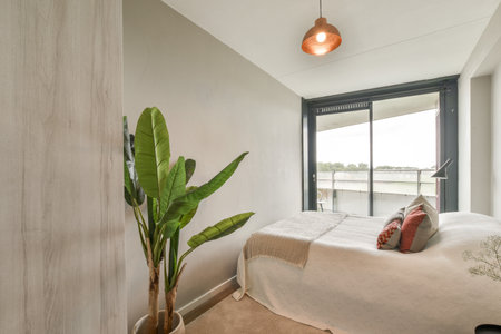 A cozy modern bedroom featuring a comfortable bed, decorative pillows, a stylish plant, and a warm...