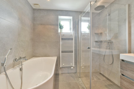 A sleek modern bathroom featuring a glass shower enclosure, a freestanding bathtub, and...