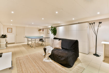 A spacious, well-lit room featuring a sofa, elegant lighting, and a ping-pong table. The decor...