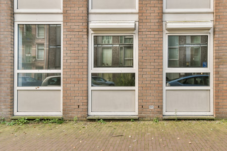 A detailed view of a modern brick building facade featuring multiple windows and reflections. The...