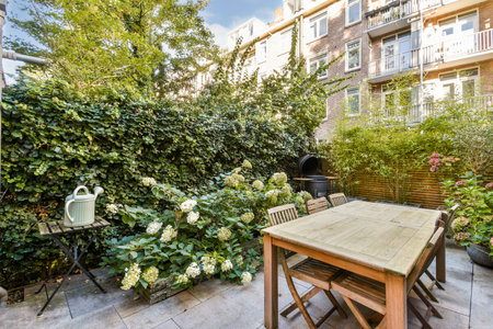 An inviting garden scene features a wooden table surrounded by lush greenery and blooming flowers,...