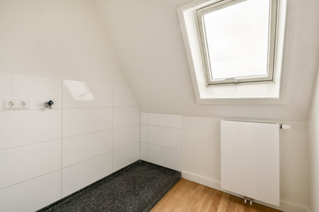 This image showcases a contemporary bathroom featuring a sloped ceiling, white tiles, and sleek heating. The minimalistic design emphasizes light and space.の写真素材