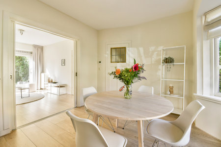 A contemporary dining area featuring a round table with white chairs, complemented by a vase of colorful flowers. Sunlight illuminates the clean, minimalist space.の写真素材