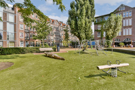 A vibrant urban playground featuring modern play equipment set within a lush green park area, surrounded by contemporary buildings and trees.の写真素材