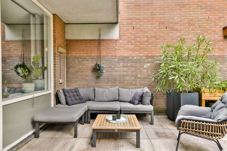 A contemporary outdoor patio setup featuring comfortable seating, decorative plants, and a brick wall, perfect for relaxation and entertaining guests.の写真素材