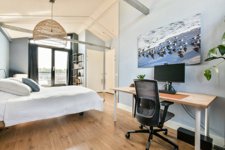 A sleek modern bedroom featuring a comfortable bed and a stylish workspace with a desk and chair. Large windows allow natural light, enhancing the calming atmosphere.の写真素材