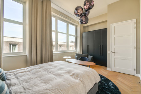 A stylish modern bedroom featuring large windows that allow natural light to flood the space,...