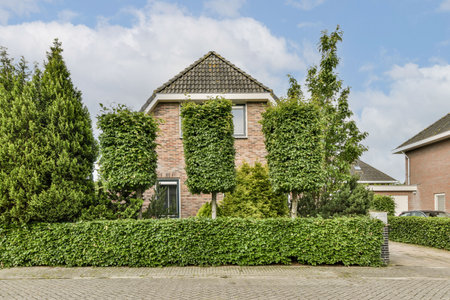A picturesque house with a brick facade, adorned by neatly trimmed hedges and vibrant greenery. The calm sky completes this tranquil suburban setting.の写真素材