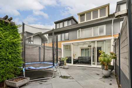 A contemporary backyard featuring a trampoline, lush greenery, and a well-designed patio area adjacent to a stylish home. Perfect for family activities.の写真素材