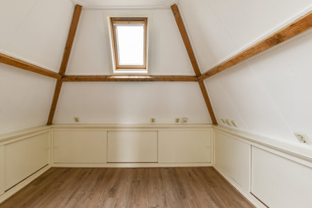 A clean, minimalist interior featuring a sloped ceiling, wooden beams, and ample natural light from...