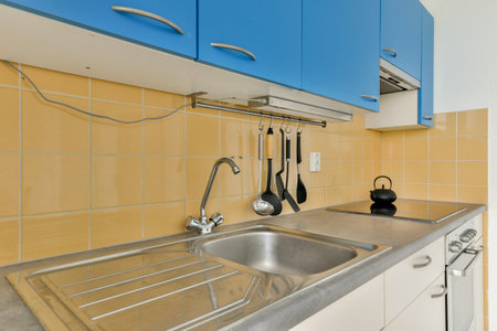 A contemporary kitchen featuring blue cabinets, stainless steel sink, cooking utensils, and a sleek...