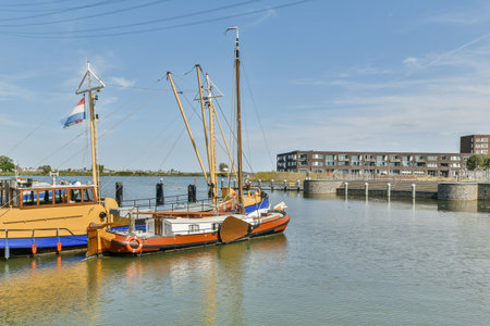 Colorful traditional boats gracefully docked at a serene harbor, reflecting the clear blue sky and the surrounding modern architecture. A picturesque waterfront scene.の写真素材