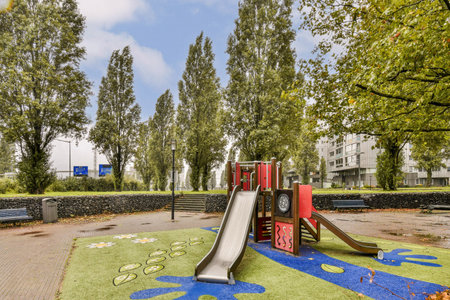 A vibrant playground featuring a red slide, surrounded by lush trees and artistic ground designs,...