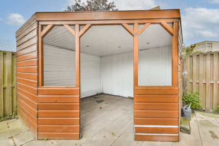 A wooden garden shed featuring an open front, showcasing a simple interior with bare walls and a stone floor, surrounded by a wooden fence and greenery.の写真素材