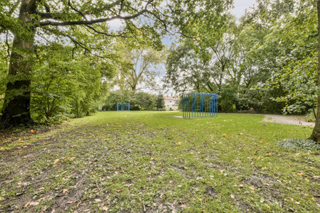 A serene park filled with green grass and trees, featuring blue playground equipment in the...