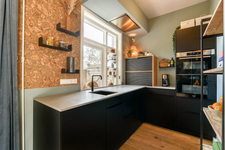 A stylish kitchen featuring sleek black cabinetry, a metallic countertop, and natural light enhancing its contemporary aesthetic.の写真素材