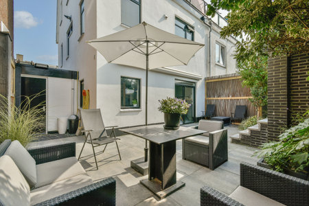 A stylish outdoor patio featuring contemporary furniture, a large umbrella, and lush greenery,...