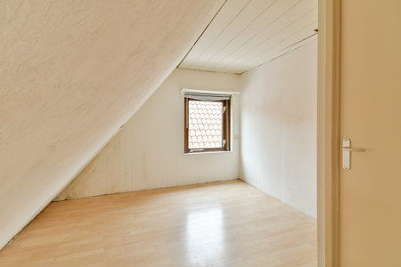 A vacant attic room featuring a sloped ceiling, wooden floor, and a single window allowing natural...