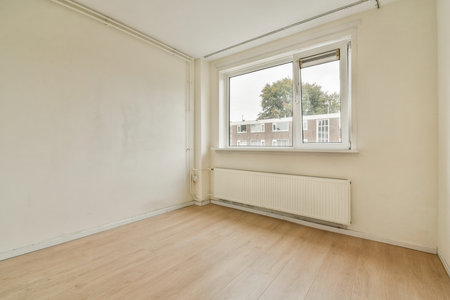 An empty room featuring a large window that offers natural light, showcasing the simplicity of indoor space with neutral tones.の写真素材