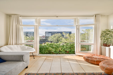A spacious living room featuring large windows that invite natural light, overlooking lush greenery. Modern furniture adds comfort to the atmosphere.の写真素材