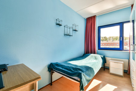 A well-lit and inviting room featuring a blue wall, a large window with curtains, and simple furniture, creating a pleasant living space.の写真素材