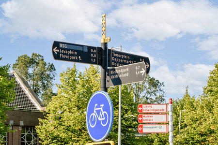 Multiple directional signs indicate various routes and locations, featuring cycling symbols and distances to nearby areas, under a clear sky.の写真素材