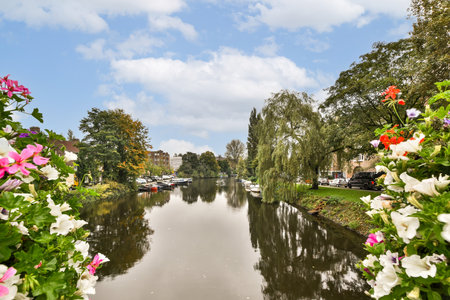 A picturesque canal view featuring lush green trees, blooming flowers, and calm water, creating a serene atmosphere perfect for relaxation and nature appreciation.の写真素材