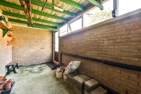 A spacious interior view of a rustic shed with exposed brick walls, green beams, and various stored items. The natural lighting enhances the simple charm of the space.の写真素材