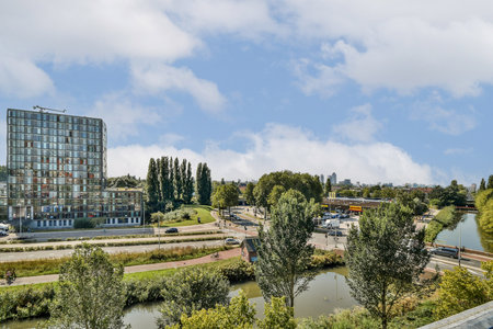 A contemporary view of an urban area featuring a modern building alongside a green park and a winding waterway, showcasing city life and natures integration.の写真素材