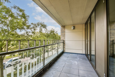 A spacious modern balcony overlooking lush greenery and a clear blue sky. The architecture features large glass windows and a sleek design.の写真素材