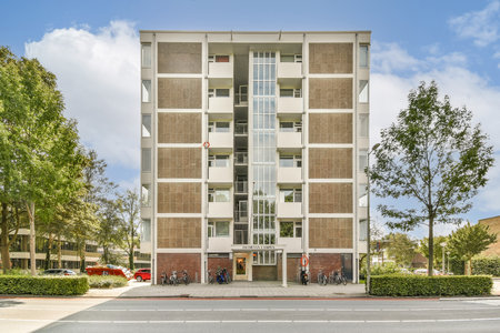 A striking modern building stands tall in an urban environment, flanked by lush trees and clear skies, showcasing contemporary architecture and urban design.の写真素材
