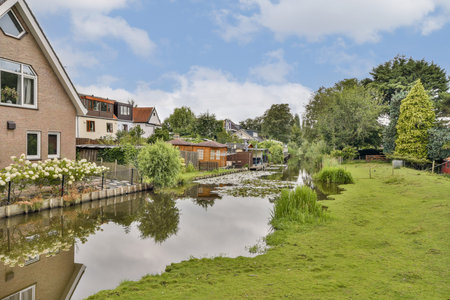 A picturesque scene showcasing a tranquil waterfront lined with lush greenery and charming homes, reflecting serene clouds and vibrant nature.の写真素材